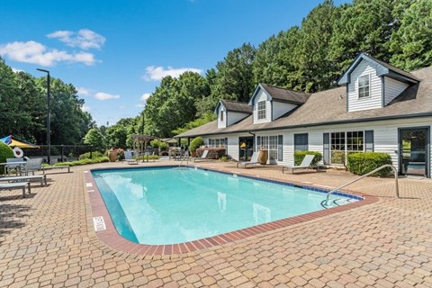 Peachtree Corners, GA, Pet-Friendly Affordable Apartments - Corners At 1700 - Outdoor Swimming Pool With Brick Paver Deck, Lounge Chairs, Clubhouse Building, And Lush Greenery View.