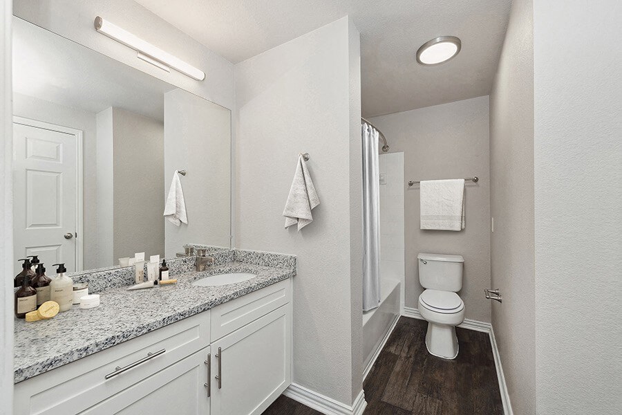 Model Bathroom with White Cabinets, Wood-Style Flooring and Shower/Tub at Chapel Hill Apartments in Lewisville, TX.