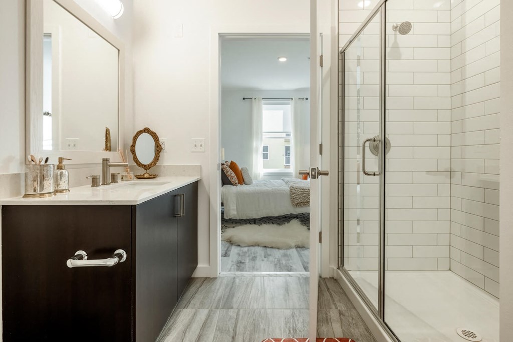 Model bathroom with a shower and a sink and a bedroom