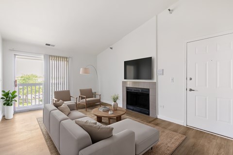 A living room with a grey sofa, a wooden coffee table, a fireplace, and a sliding glass door leading to a balcony.