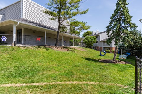 Community dog park with 2 trees, grass, and dog tunnel.