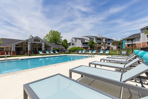 Community pool with sun loungers and a table in the foreground with apartment buildings in the background.