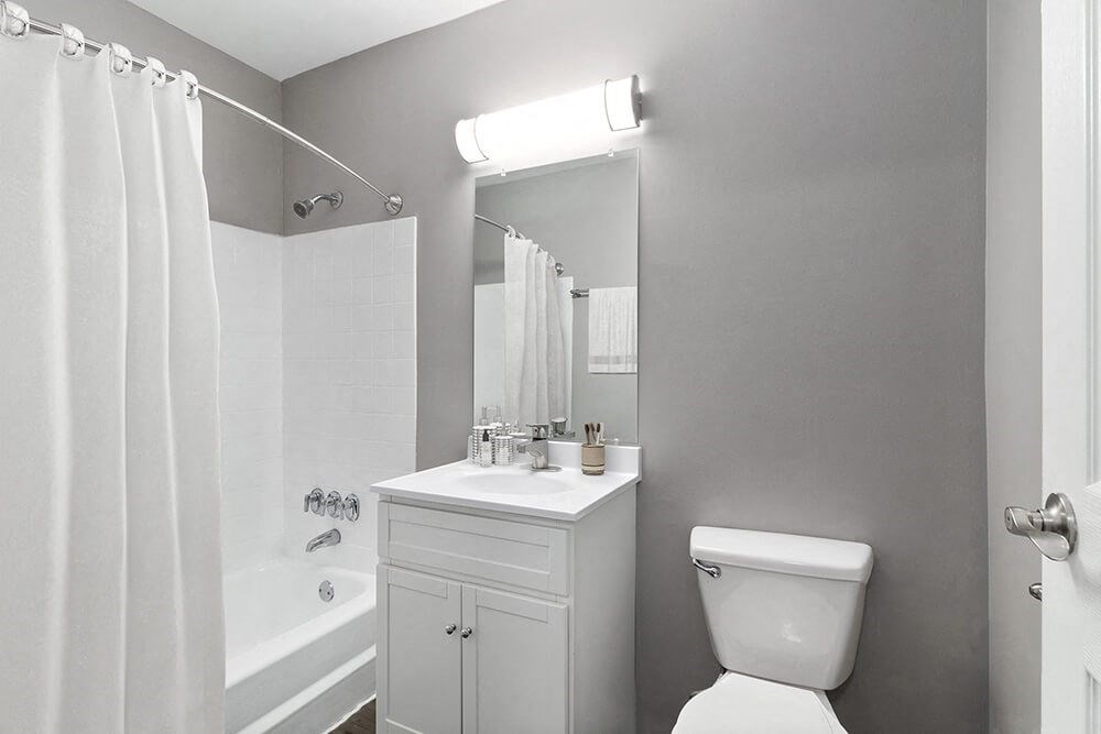 Model Bathroom with White Cabinets, Wood-Style Flooring and Shower/Tub at Midpointe Apartments in Chicago, IL.