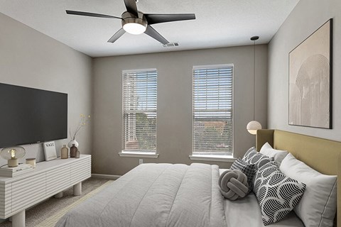 2-Bedroom Luxury Apartments in Marietta, GA - Parkside at Town Center - Modern Bedroom With Upholstered Headboard, Ceiling Fan, Dual Windows With Blinds, And Wall-Mounted Television On Dresser.