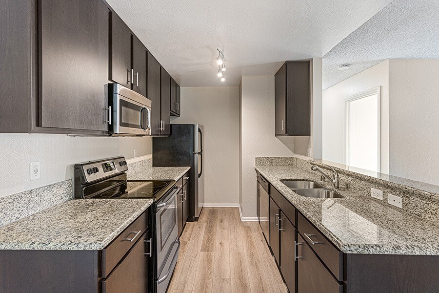 Model Kitchen with Dark Wood Cabinets and Wood-Style Flooring at Santa Fe Ranch Apartments located in Carlsbad, CA.