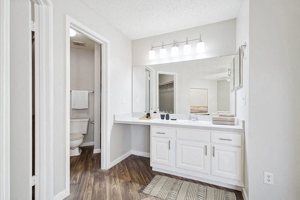 Attached Model Bathroom with White Cabinets and Wood-Style Flooring at Westland Park Apartments in Jacksonville, FL.