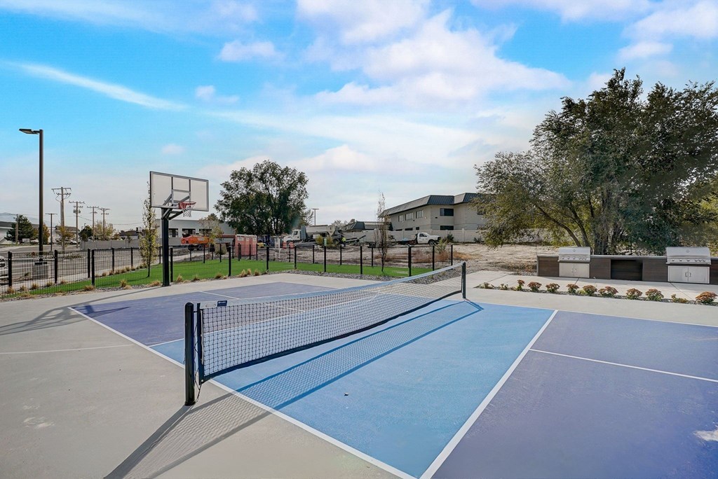 A tennis court with a net and a basketball hoop in the background.