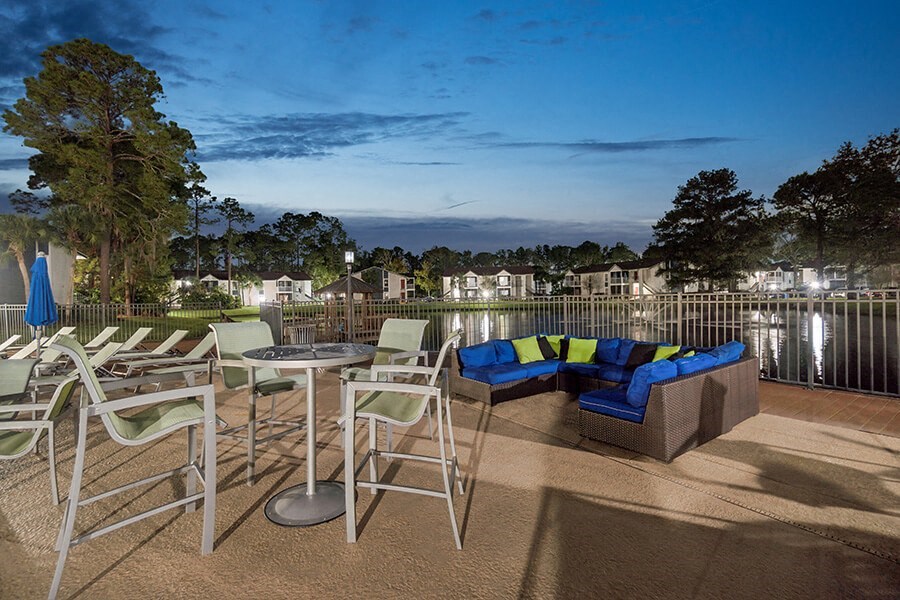 Outdoor BBQ Area with Lounge Furniture and View of Community Lake at Vue at Baymeadows Apartments located in Jacksonville, FL.