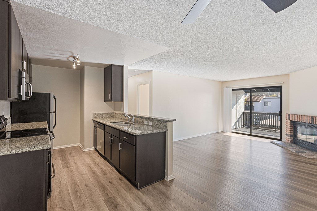 Model Kitchen with Dark Wood Cabinets, Wood-Style Flooring and Patio Accessibility at Santa Fe Ranch Apartments located in Carlsbad, CA.
