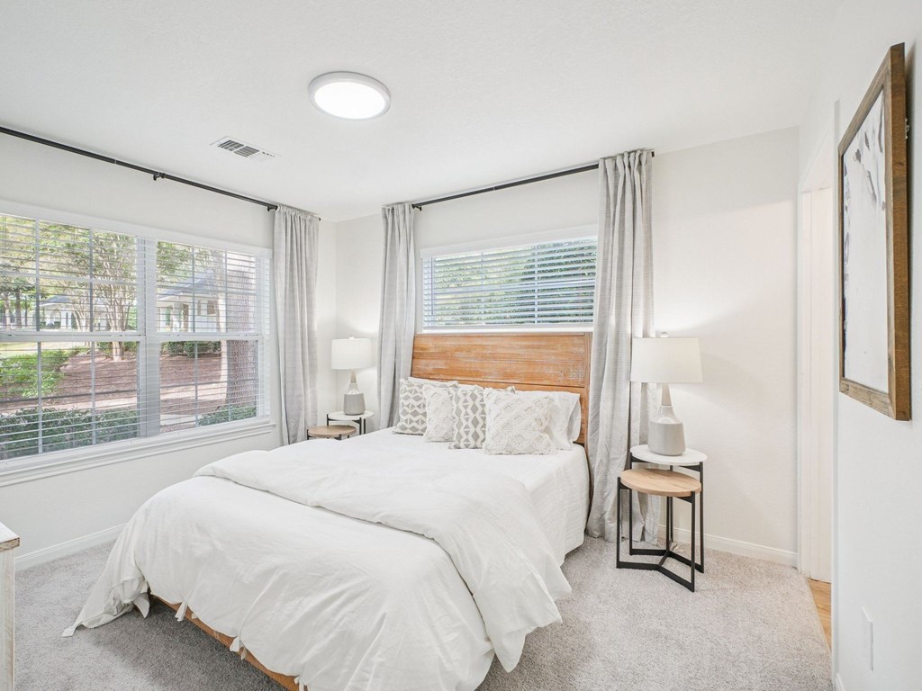 A bedroom with a large bed and a window with white curtains.