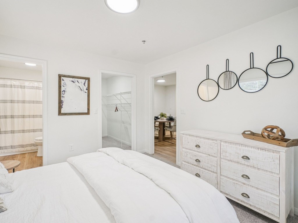 A white bedroom with a large bed and a white dresser.