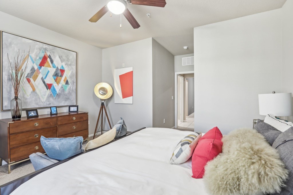 Model bedroom with a bed, a dresser, and a ceiling fan.