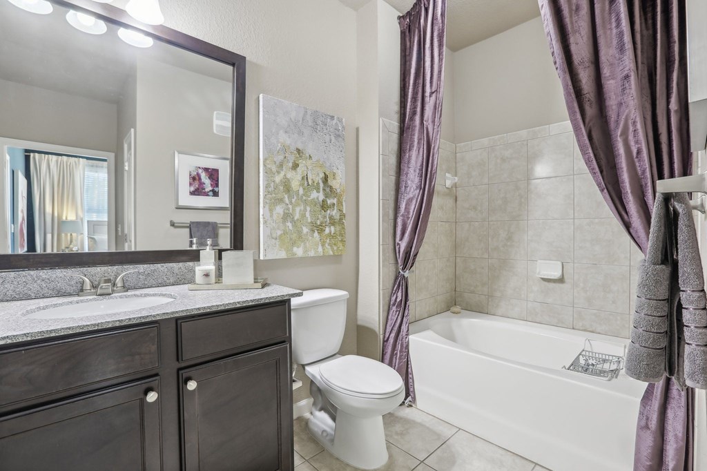 Model bathroom with a white toilet, a white bathtub, and a large mirror.
