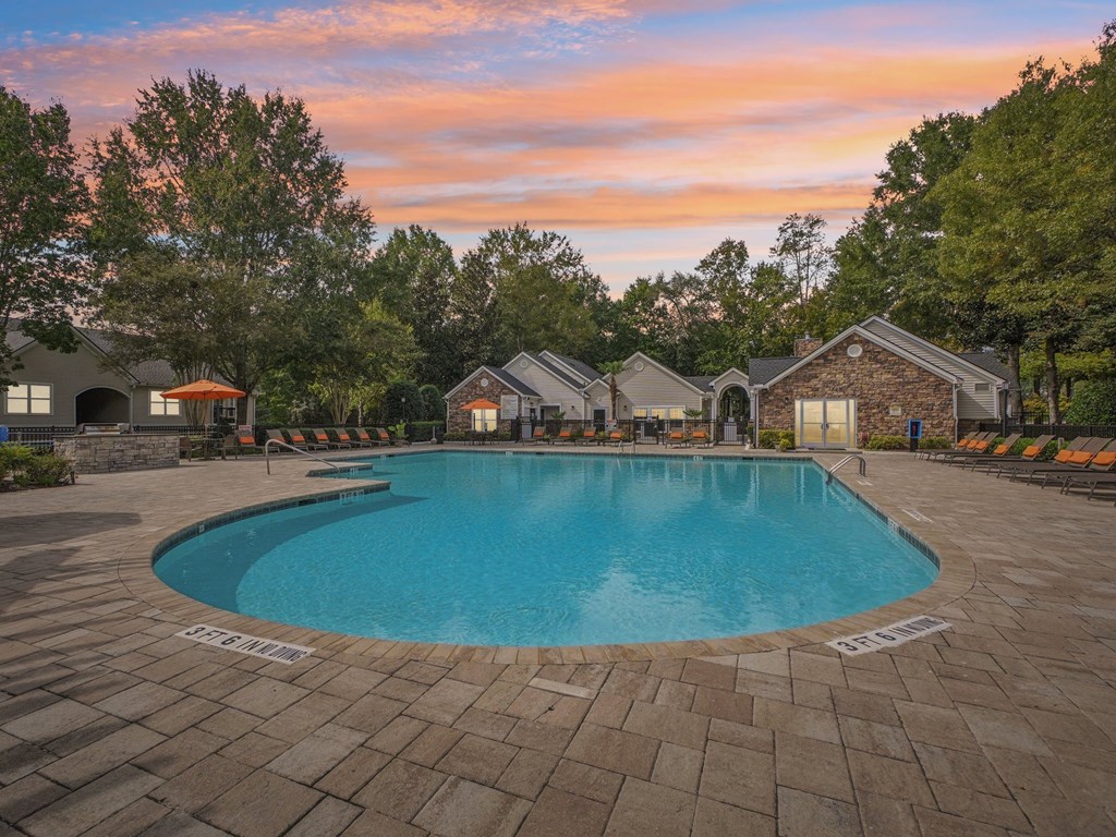 A large swimming pool surrounded by a brick patio and lounge chairs.
