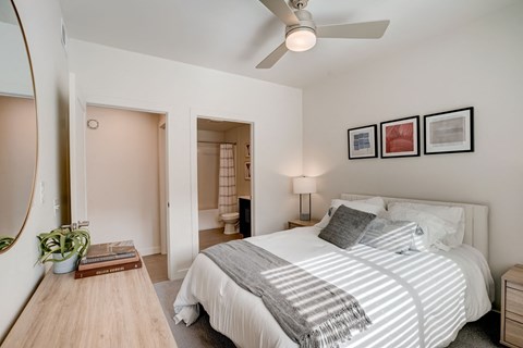 West Valley City, UT, Pet-Friendly Apartments - Sage Valley - A Bedroom With A White Bed, Ceiling Fan, Nightstand Lamp, Framed Wall Art.