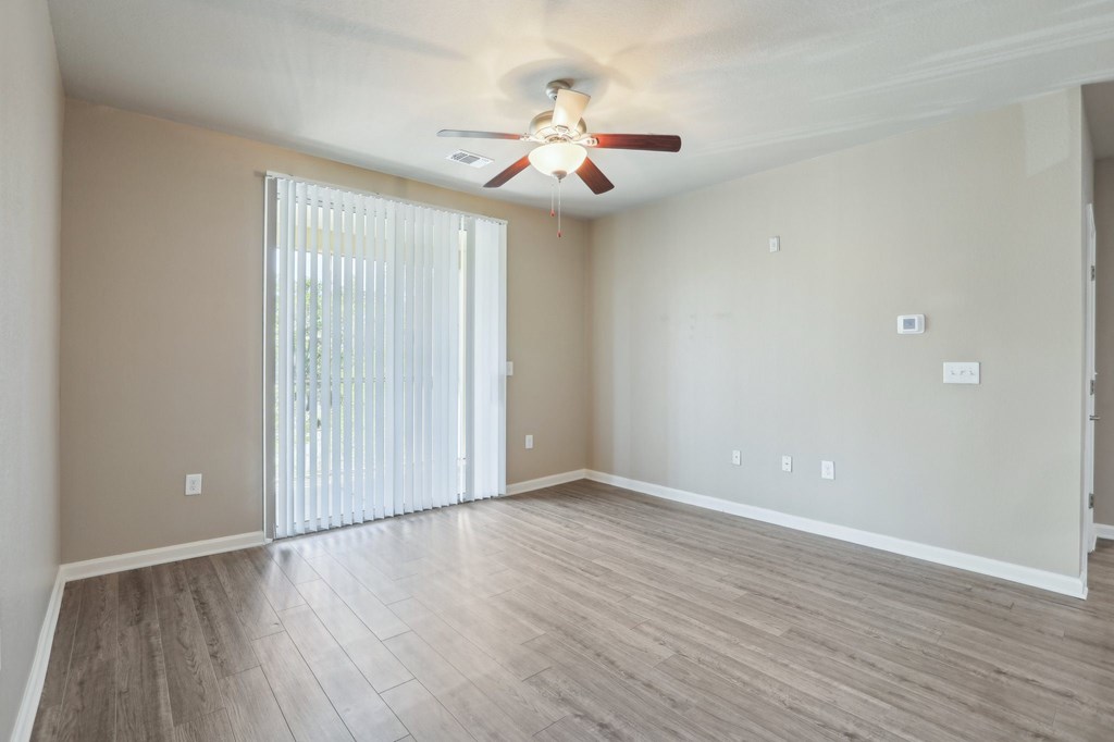 Model living room with a ceiling fan and sliding glass doors.
