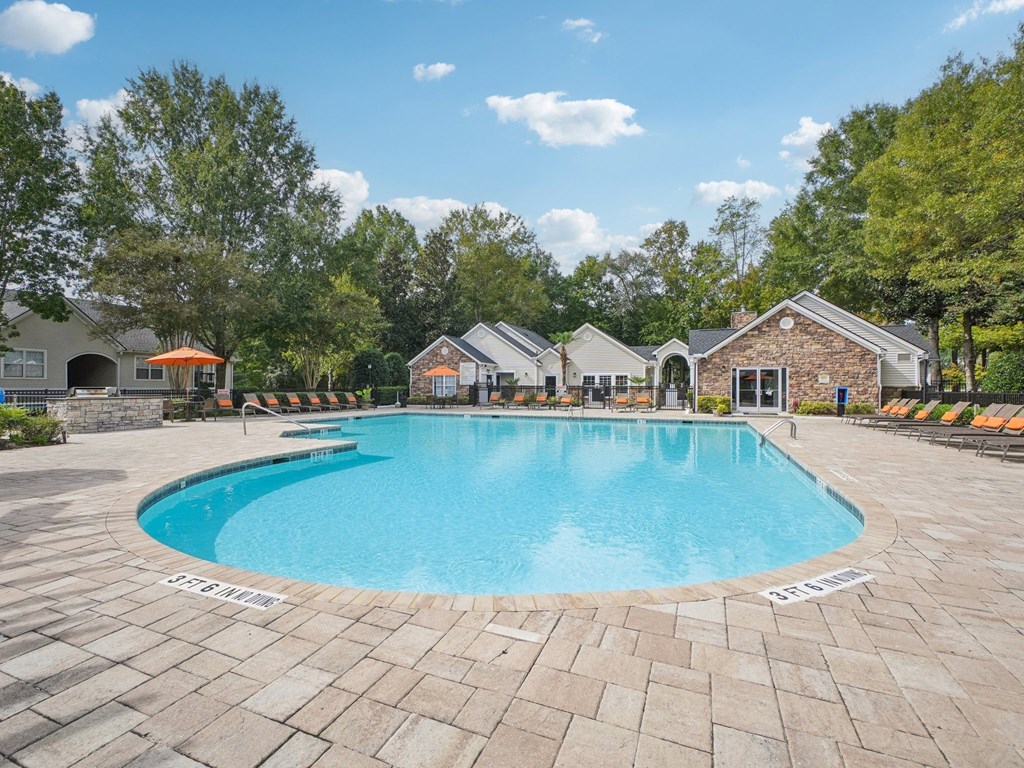 A large outdoor swimming pool surrounded by a brick patio and lounge chairs.