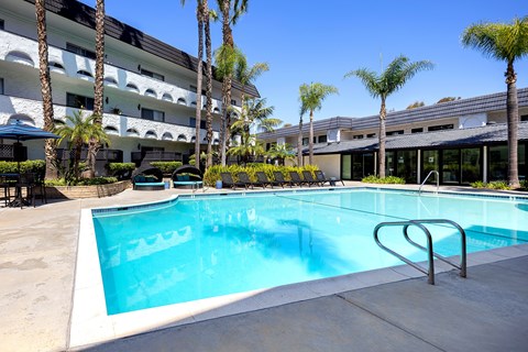 A swimming pool in front of a building with palm trees.