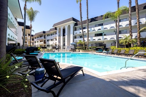A pool surrounded by lounge chairs and palm trees.