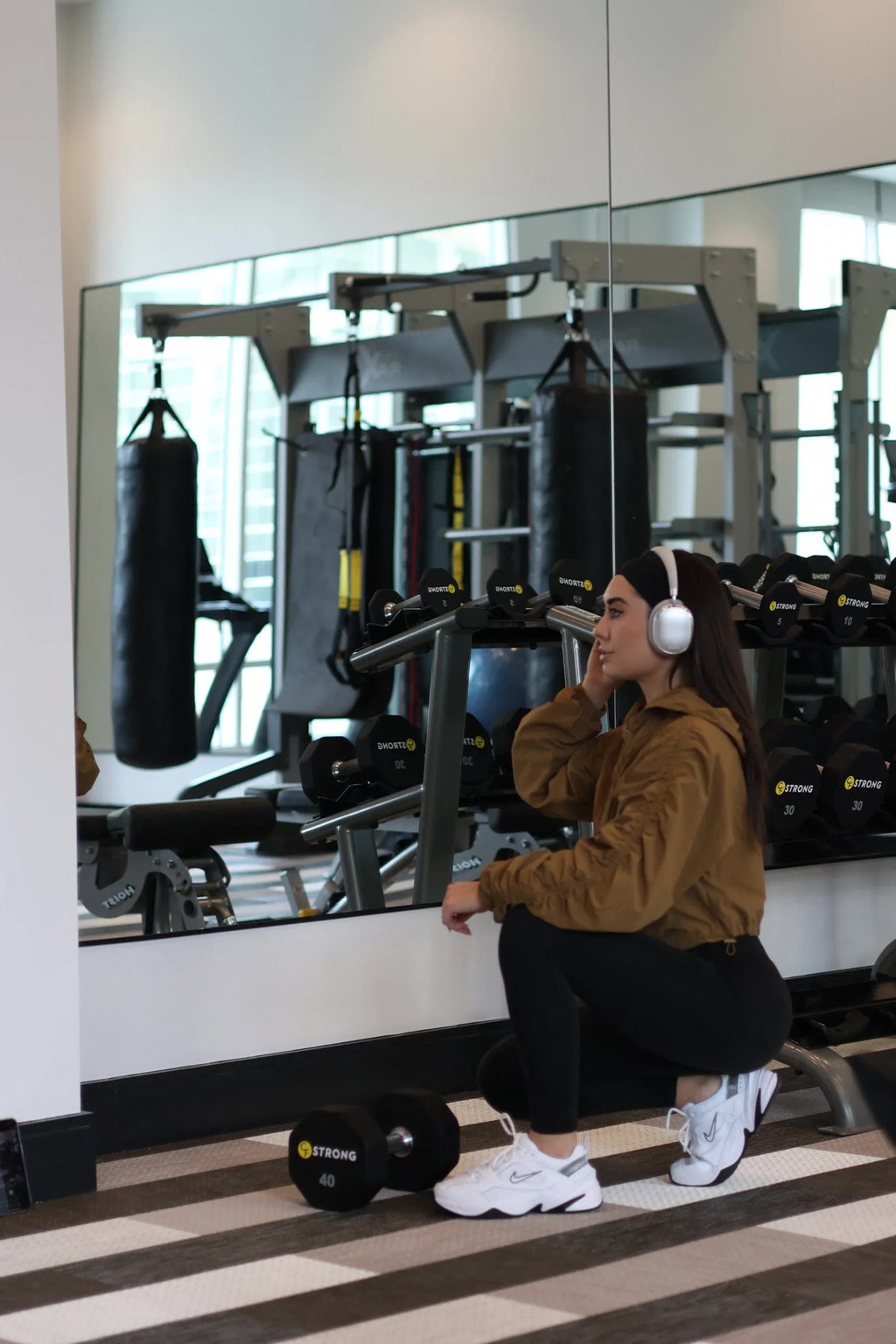 a woman sitting on a bench in a gym with headphones on