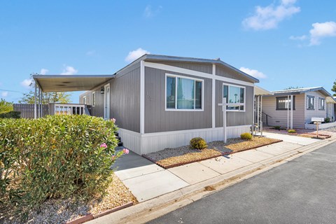 A grey house with a white fence and bushes in front.