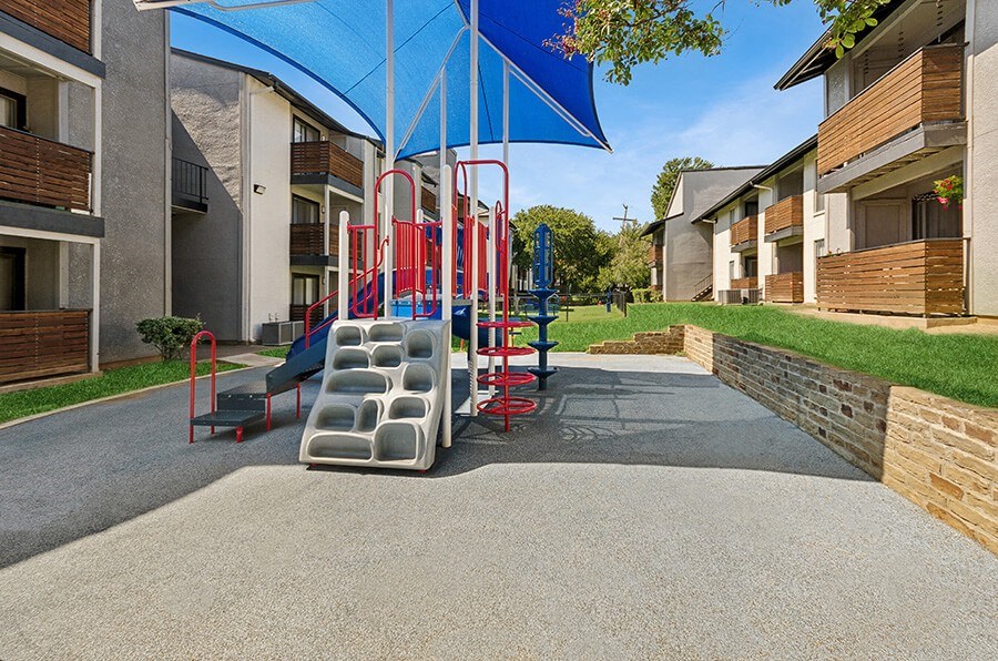 Community Playground with Slide and Blue Canopy at Summit Ridge Apartments located in Arlington, TX.