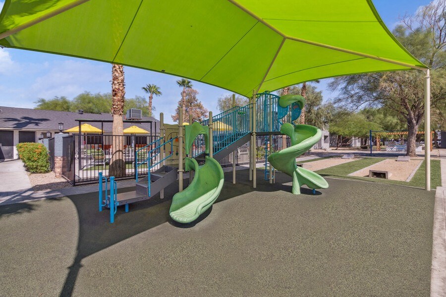 a playground with slides and a swing set under a green canopy