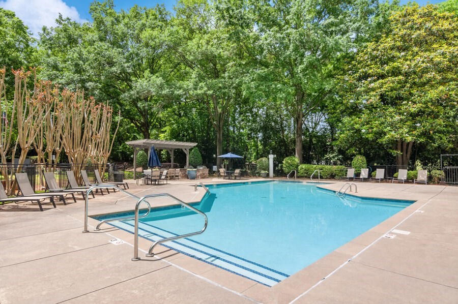 a swimming pool with chaise lounge chairs and trees in the background