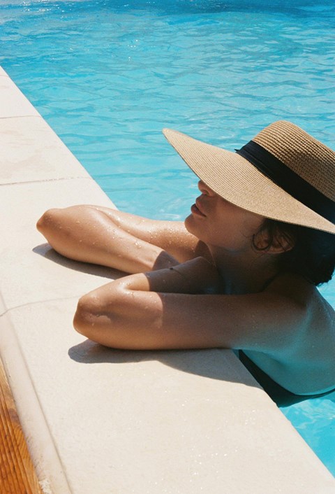 A person in a hat is sitting by a pool.