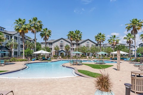 A swimming pool surrounded by palm trees and a resort-style building.