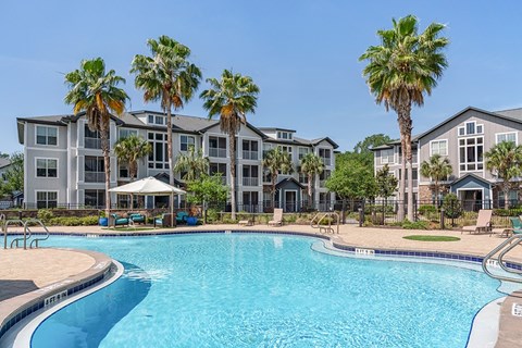 A swimming pool in front of a building with palm trees.