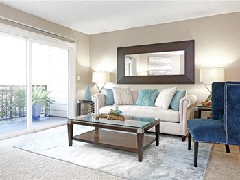 Staged apartment living room with couch, coffee table, and chair, includes a balcony. - Photo Gallery 3