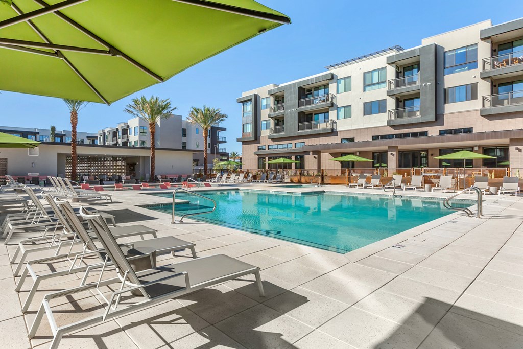 a swimming pool with lounge chairs and umbrellas in front of an apartment building