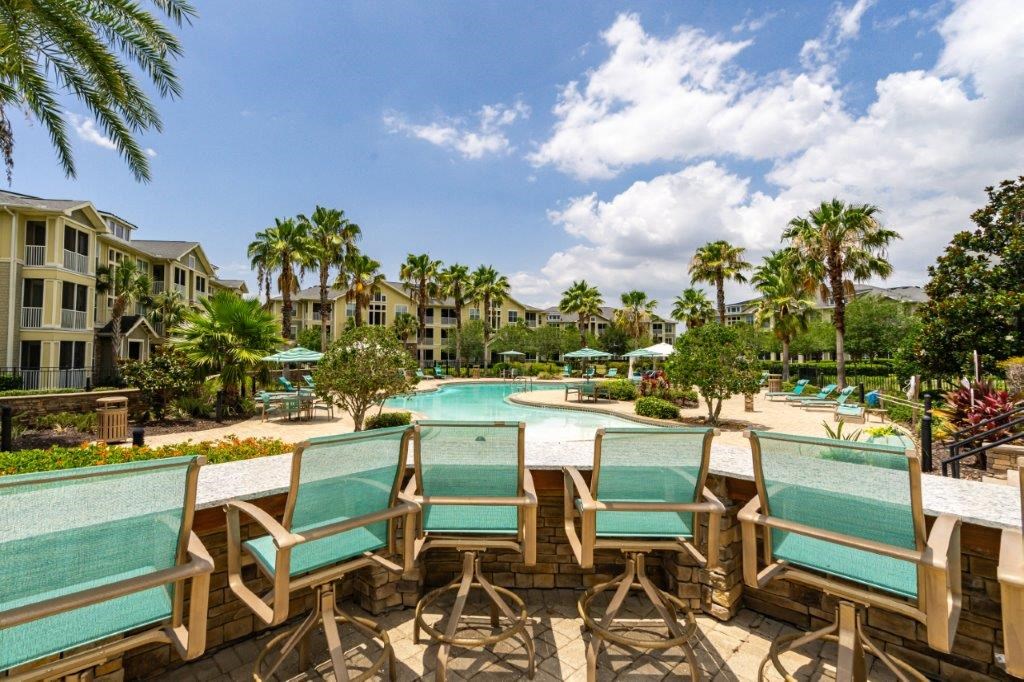 Pool surrounded by wooden chairs and palm trees at Bridges at Crosstown in Tampa, FL