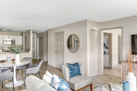 A living room with a grey couch and a round mirror on the wall.