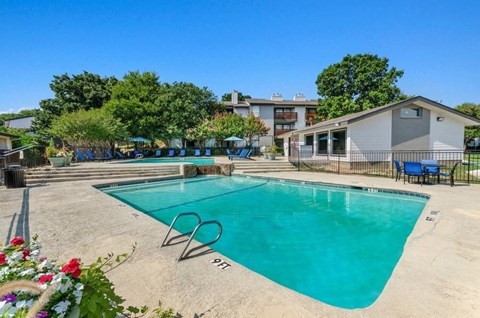 Arlington, TX, Pet-Friendly Apartments - Woodcreek - Outdoor Swimming Pool With Wide Sundeck, Lounge Chairs, Clubhouse Building, Mature Trees, And Clear Blue Sky.
