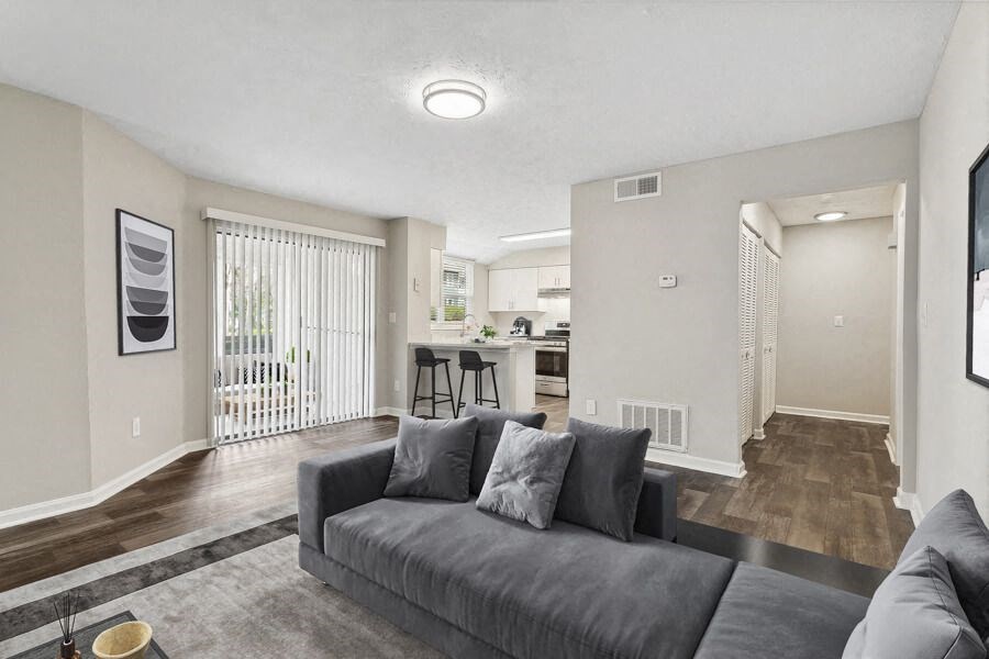 Model apartment living room with a couch and a kitchen in the background