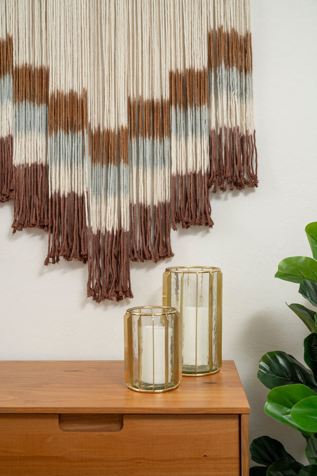 a piece of artwork hangs on a wall next to a table with two candles and a plant