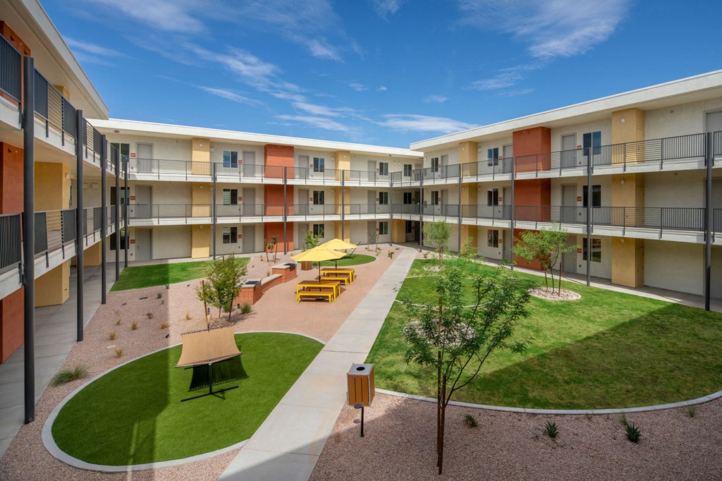 a courtyard with grass and tables and chairs in the middle of an apartment complex