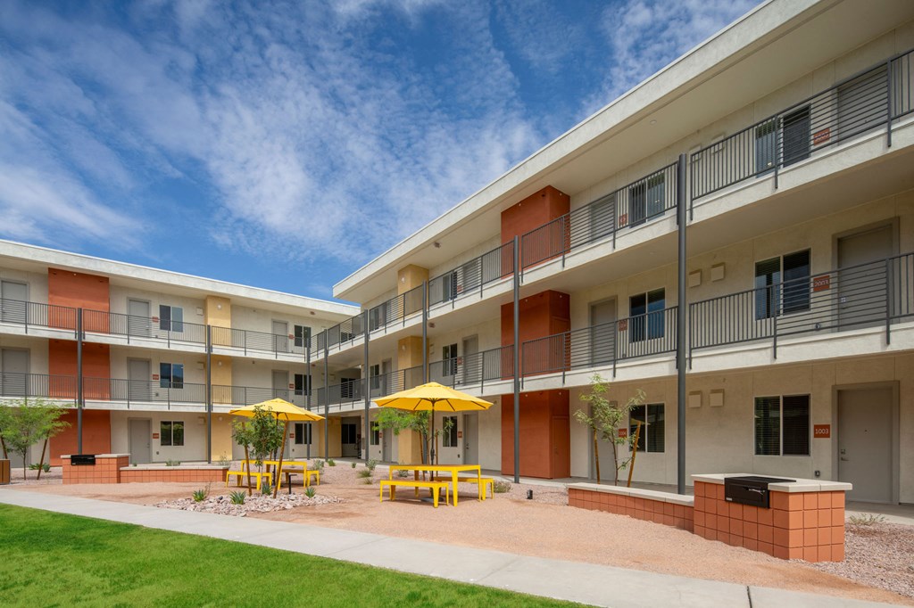 a courtyard with yellow tables and yellow umbrellas in front of an apartment building
