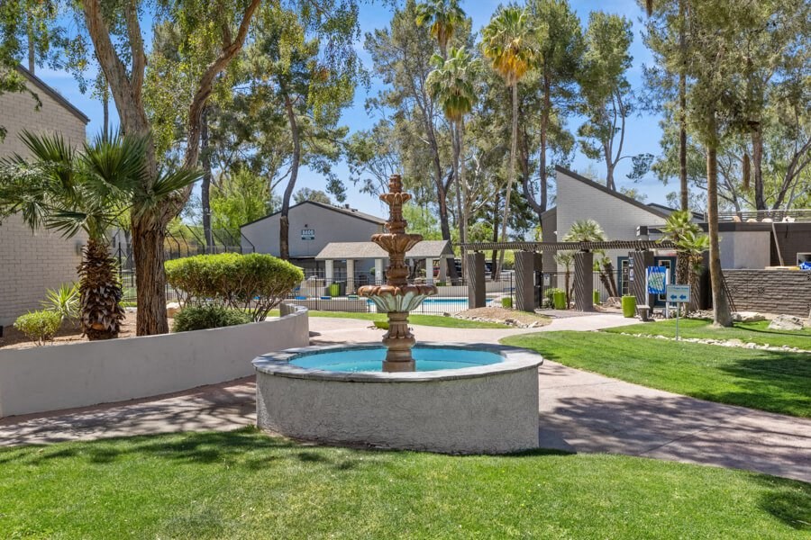a fountain in the middle of a grassy area with apartments in the background