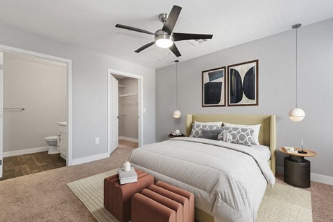 Three-Bedroom Modern Apartments in Surprise, AZ - Harmony at Surprise - A Bedroom With A Large Bed With Neutral Bedding, Ceiling Fan, Pendant Lights, And Abstract Wall Art.