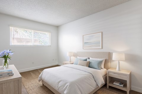 A bedroom with a large bed, a nightstand with a lamp, and a painting on the wall.