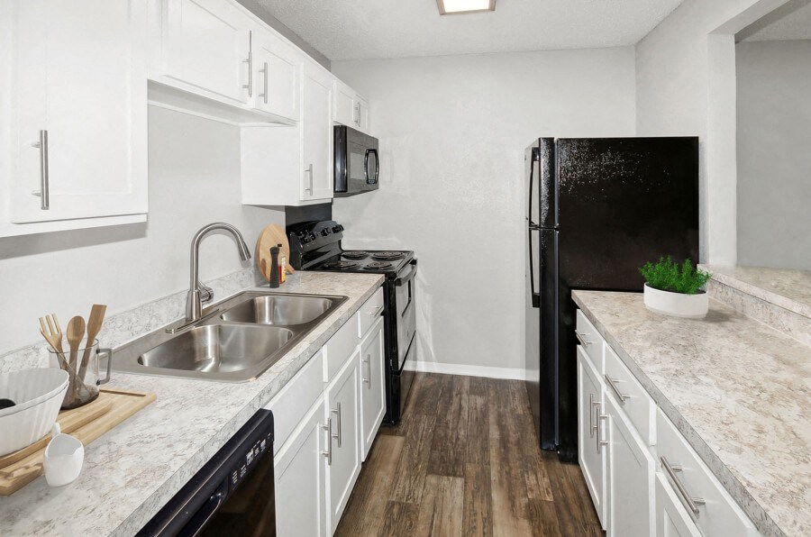 Model apartment kitchen with white cabinets and a black refrigerator