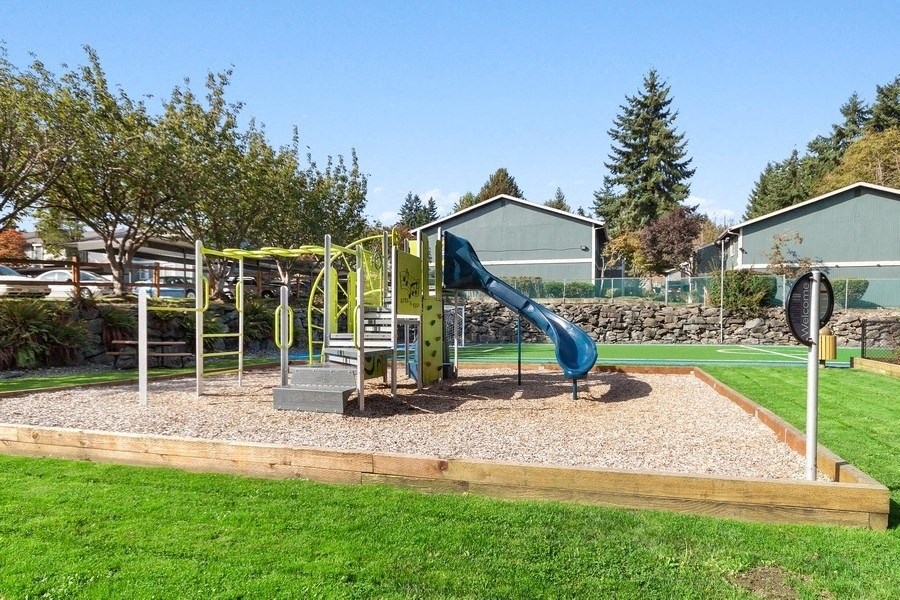 Playground in boxed in area full of sand surrouned by lush green landscape