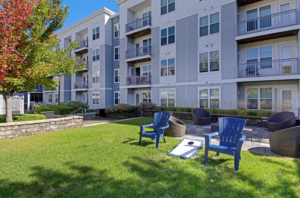 A sunny day at a grassy courtyard with blue chairs and a white building in the background.