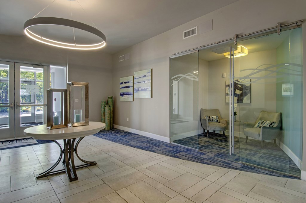 A white table with a black base is in the middle of a room with a glass wall and a mirror.