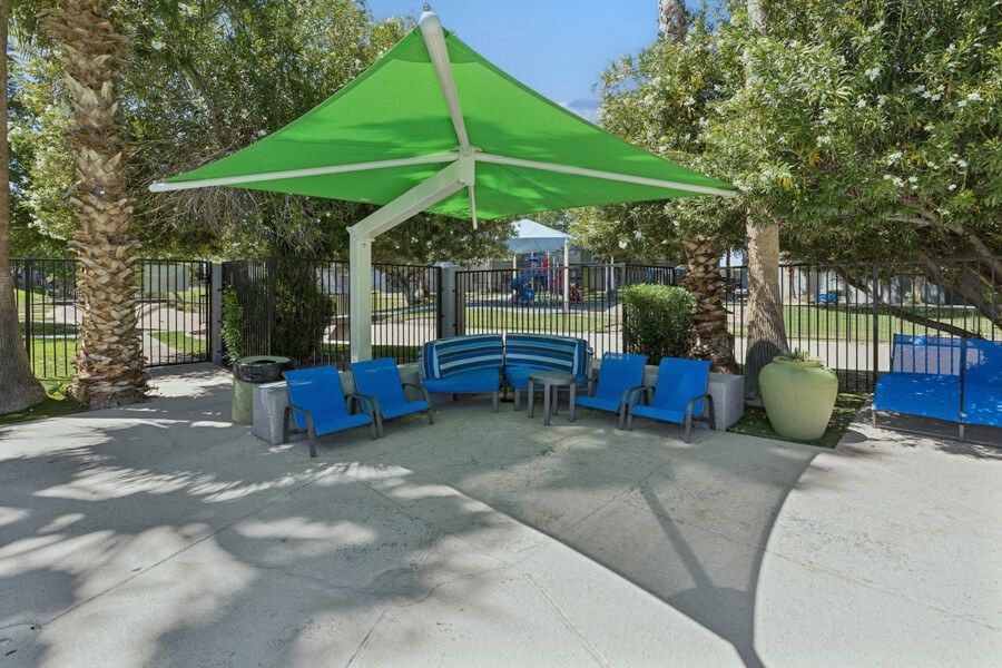 a picnic area with blue chairs and a green umbrella in a park