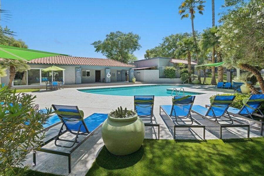 a swimming pool with blue lounge chairs and the clubhouse in the background