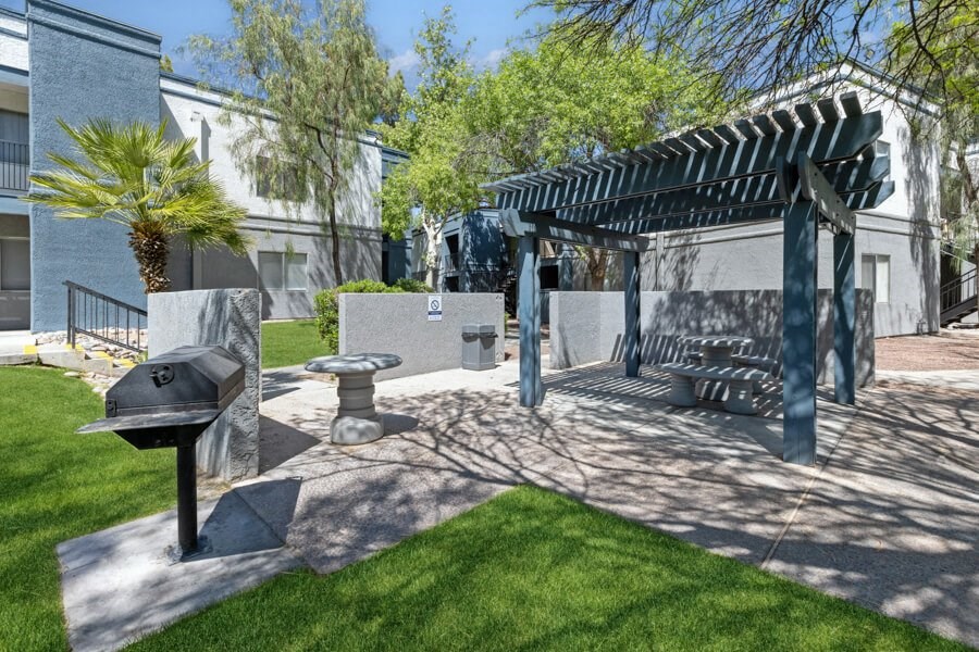 a patio with a grill and a pergola in front of a building